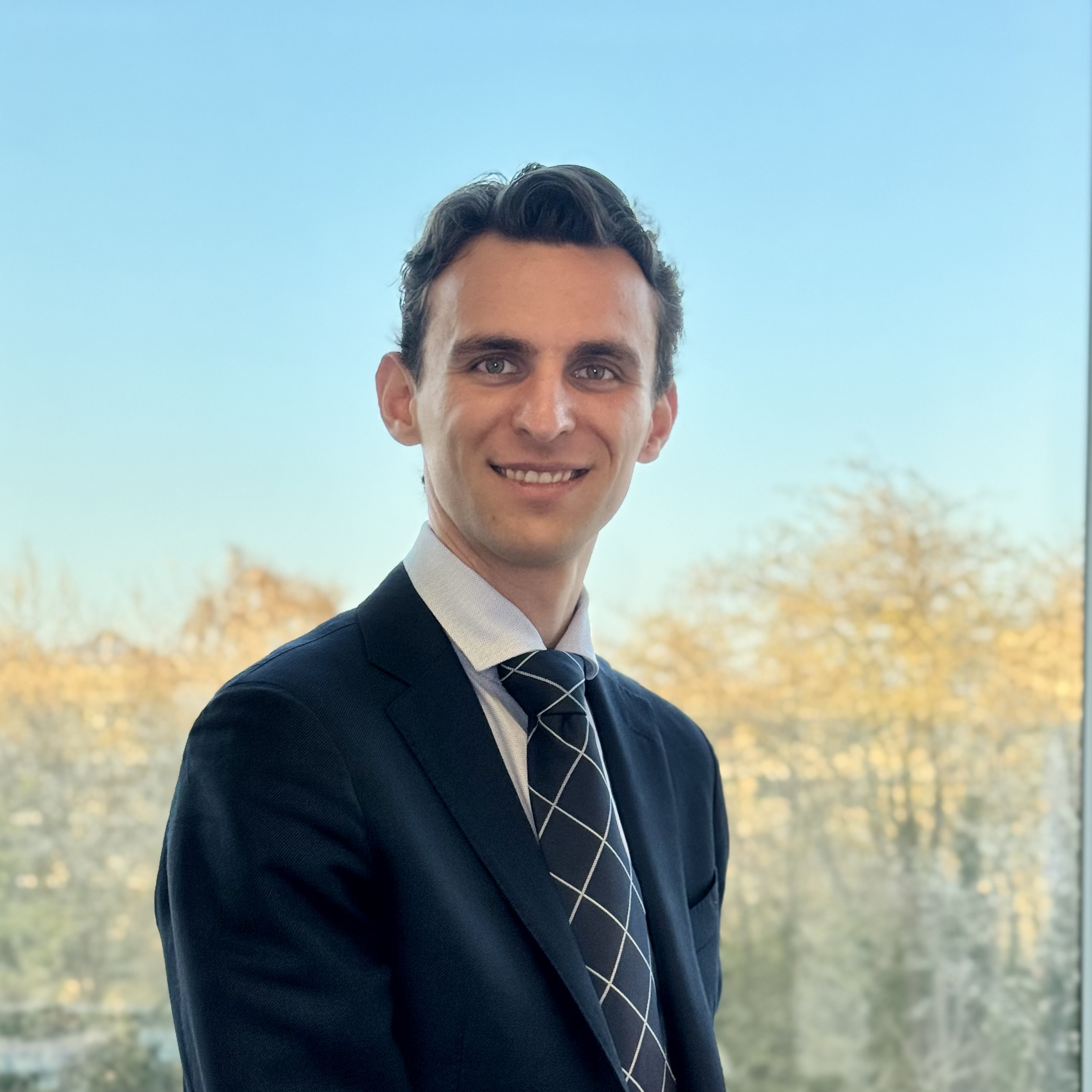 Portrait of Tibo Vanleke smiling in a navy suit and tie.